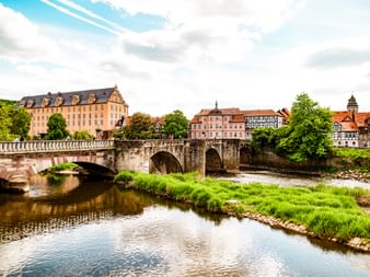 Old stone arch bridge crossing a river in Hann. Münden with historic buildings and half-timbered houses along the waterfront under a blue sky.