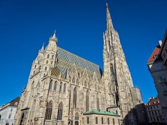 St. Stephen's Cathedral in Vienna with its tall Gothic spire and distinctive patterned roof against a clear blue sky.