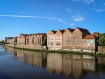 Weserburg Museum für moderne Kunst in Bremen mit historischen Backsteingebäuden, die sich in der Weser unter blauem Himmel spiegeln.