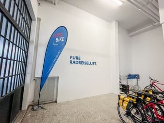 Helles weißes Büro in Bozen mit Eurobike-Tropfenfahne und Slogan 'Pure Radreiselust' an der Wand. Fahrräder im Hintergrund sichtbar.