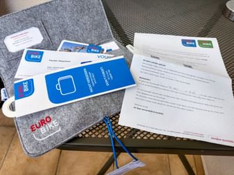 Gray felt folder with Eurobike logo containing travel documents, blue bike vouchers, and information sheets for Meran-Gardasee cycling tour.