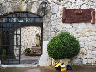 Steineingang mit gewölbter Glastür mit der Aufschrift 'Monnaber Nou' und Kupferschild 'Monnaber Nou Hotel-Restaurant'. Ein gelber Roller ist darunter geparkt.