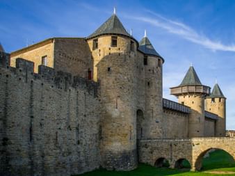 Steinfestung in Carcassonne mit runden Türmen mit Kegeldächern und Steinbrücke. Mittelalterliche Mauern unter blauem Himmel.