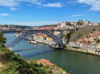 Doppelstöckige Metallbogenbrücke Ponte Luís I über den Douro in Porto mit historischen Altstadtgebäuden am Hang und Booten im Wasser.
