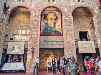 Innenhof des Dalí-Museums mit Ziegelwänden, gewölbten Nischen und pixeliertem Porträt. Besucher betrachten Kunstwerke in Katalonien.