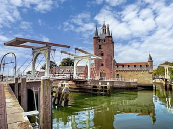 Alter Hafen von Zierikzee mit weißer Zugbrücke über grünem Wasser, roter Backsteinkirchturm mit Spitze im Hintergrund unter blauem Himmel.