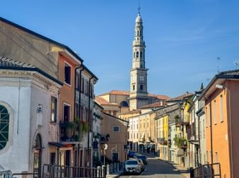 Street view in Monteforte d'Alpone with colorful buildings and a tall church bell tower rising above the town under a clear blue sky.