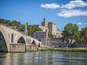 Historische Steinbrücke mit Bögen über die Rhône in Avignon, mit dem mittelalterlichen Papstpalast und Festungsmauern im Hintergrund.