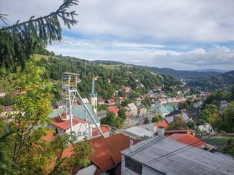 Historischer Förderturm Svornost überblickt die Stadt Sankt Joachimsthal mit rotgedeckten Gebäuden inmitten bewaldeter Hügel des Erzgebirges.