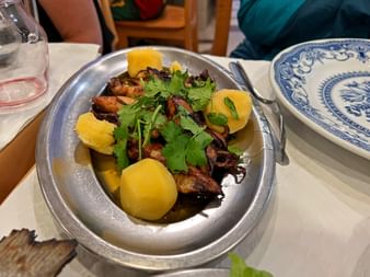 Gegrillte Scampi mit frischem Koriander und Zitronenscheiben in einer Metallpfanne auf weißer Tischdecke mit blau-weißen Tellern.