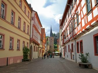 Kopfsteinpflasterstraße in Karlstadt Altstadt gesäumt von bunten Fachwerkhäusern und einem mittelalterlichen Turm mit Spitze im Hintergrund.