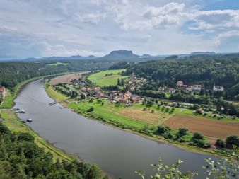 Panoramic view from Bastei over the Elbe River winding through Kurort Rathen. Green fields, forests, and distinctive table mountains of Saxon Switzerland.