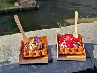 Zwei belgische Waffeln auf Papptellern an einem Kanal in Brügge. Linke Waffel mit Schokolade und Nüssen, rechte mit Erdbeeren und Sahne.