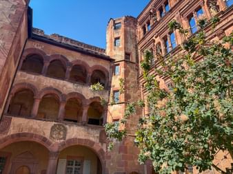 Innenhof des Heidelberger Schlosses mit dem Ottheinrichsbau mit Renaissance-Arkaden und verzierter Fassade neben einem Ruinenturm mit grüner Vegetation.