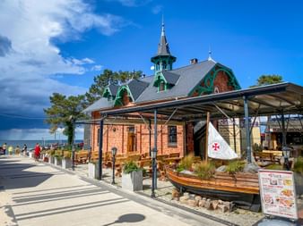 Red brick building with green decorative elements and tower on seaside promenade in Misdroy. Wooden boat and outdoor seating visible in front.