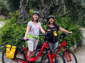 Two women with e-bikes in front of a tree