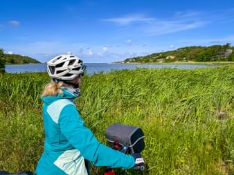 Cyclist in turquoise jacket with white helmet viewing blue water and green coastline at Hördalens nature reserve in Sweden.