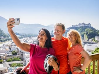 2 women and 1 man taking a selfie with Hohensalzburg Fortress in the background