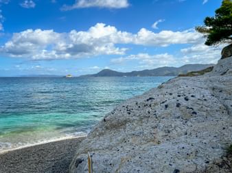 Padulella Beach on Elba with turquoise water, white rocky shore, and mountains in the distance under a blue sky with white clouds.