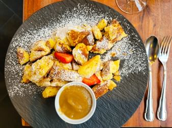 Kaiserschmarrn on a dark plate, dusted with powdered sugar and garnished with strawberry slices. A small bowl of applesauce sits in the center.