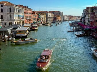 Blick auf den Canale Grande in Venedig mit Wassertaxis und Booten zwischen bunten historischen Palästen unter blauem Himmel.