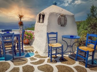 Weiß getünchte Tavernenterrasse auf Kreta mit blauen Holzstühlen, runden Tischen und gemustertem Boden mit Meerblick.