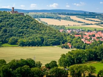 Panoramic view of Drei Gleichen castle ruins on a forested hill above a village, with rolling fields and distant mountains in Thuringia.