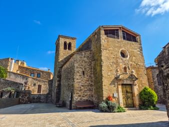 Mittelalterliche Steinkirche mit Glockenturm in Peratallada, Katalonien. Das romanische Gebäude hat goldene Steinmauern und einen Holzeingang.