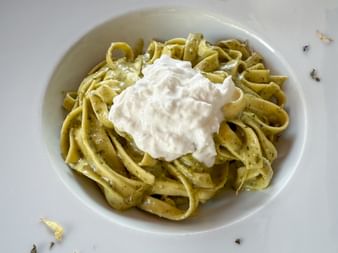 Weiße Schüssel mit Linguine in grüner Pestosauce, garniert mit cremigem weißem Burrata-Käse, serviert in Venedig.
