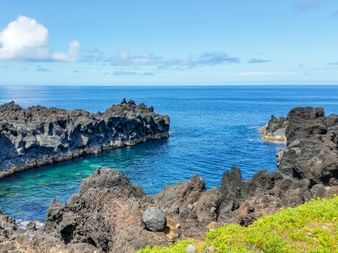 Naturpool umgeben von dunklen vulkanischen Lavafelsen an der Küste von Flores. Türkisfarbenes Wasser füllt den Pool, mit tiefblauem Ozean und Himmel.