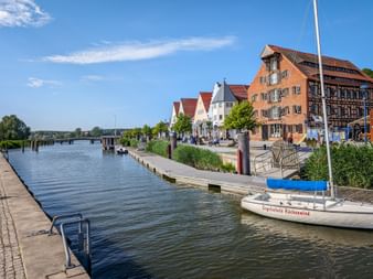 Waterfront promenade in Wolgast with sailboat moored in canal. Historic buildings line the harbor, including timber-framed houses under blue sky.