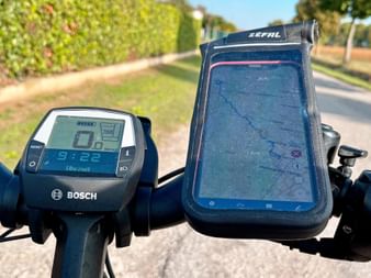 Bicycle handlebar with Bosch display showing 9:22 and a Zefal phone holder containing a smartphone with a map on a tree-lined cycling path.