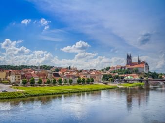 Historic town of Meissen along the Elbe River with Albrechtsburg castle and cathedral on the hilltop under blue sky with white clouds.