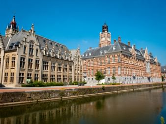 Historische Gebäude entlang eines Kanals in Dendermonde mit prächtiger Architektur, roten Backsteinfassaden und grauen Schieferdächern unter blauem Himmel.