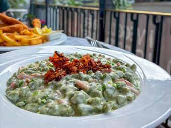 Green spinach spätzle with ham pieces and crispy fried onions on top, served on a white plate. French fries visible in the background.