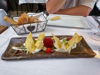 Elegante Vorspeise auf Holzbrett mit Käse, knusprigen Waffeln, Erdbeeren und Microgreens. Brotkorb und weiße Teller im Hintergrund.