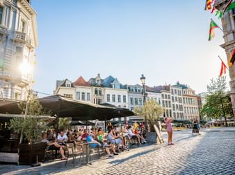 Sonnige Terrassenszene am Grote Markt in Antwerpen mit Menschen, die draußen speisen. Bunte historische Gebäude säumen den Kopfsteinpflasterplatz.