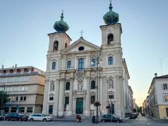 White baroque church with twin green onion domes in Gorizia. The St. Ignatius Church facade features ornate sculptures and arched windows.