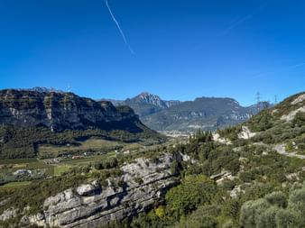 Winding mountain pass road near Nago with rocky cliffs, green vegetation, and mountain ranges under clear blue sky.
