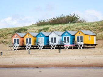 Reihe von sechs bunten Strandhütten in Orange, Gelb, Blau und Weiß am Sandstrand mit Dünengras in Vlissingen, Zeeland.