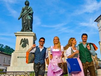 Four people in traditional costume in front of the Mozart statue