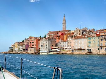 View from boat of Rovinj's colorful waterfront buildings and church bell tower in Istria, Croatia, under blue sky.