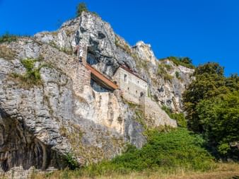 Stone chapel built into the limestone cliff face of Isteiner Klotz in the Southern Black Forest, surrounded by green vegetation under blue sky.