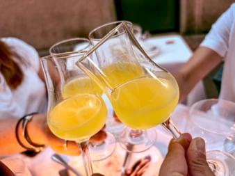 Three glasses filled with yellow limoncello clinking together in a toast during a cycling trip from Meran to Lake Garda in Trient.