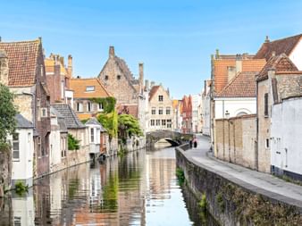 Malerischer Kanal in Brügge gesäumt von mittelalterlichen Gebäuden mit Treppengiebeln und orangen Ziegeldächern. Eine Steinbrücke überquert den Kanal.