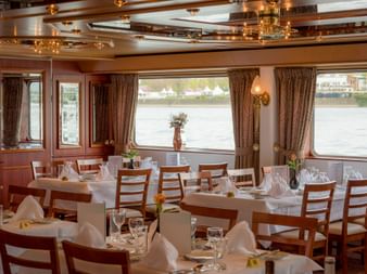 Elegant dining room aboard MS Switzerland with white-clothed tables, wooden chairs, and large windows overlooking the river.