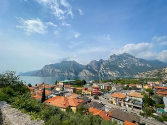 Panoramablick auf Torbole am Gardasee mit bunten Häusern, dramatischen Bergen am blauen See und klarem Himmel darüber.