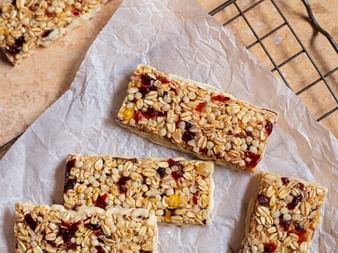 Four homemade muesli bars with oats and dried fruit on parchment paper placed on a black wire cooling rack.