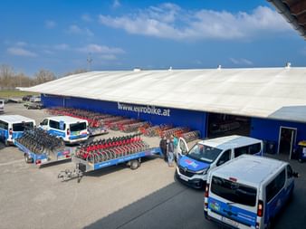 Aerial view of Eurofun facility with trailers loaded with red bicycles and blue company vans parked in front of a warehouse with eurobike.at signage.