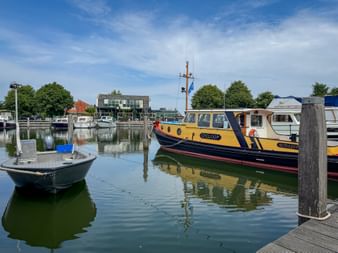 Yellow boat named Cycloop moored at Broekerhaven harbor on the IJsselmeer, with a small rowboat in the foreground and buildings visible in the background.